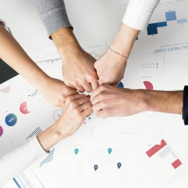 Free Colleagues celebrate success with a fist bump over financial charts depicting teamwork and unity. Stock Photo