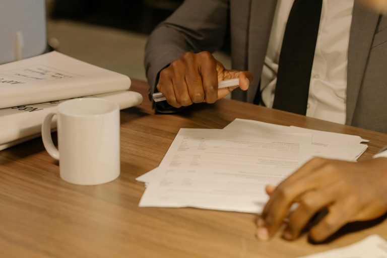 Cyber insurance renewal: Free Close-up of a businessman holding and reviewing documents on a wooden desk. Stock Photo