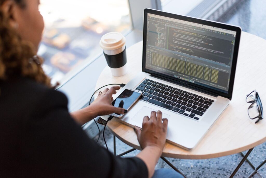 Woman typing on a laptop showing code with a smartphone and coffee on the table